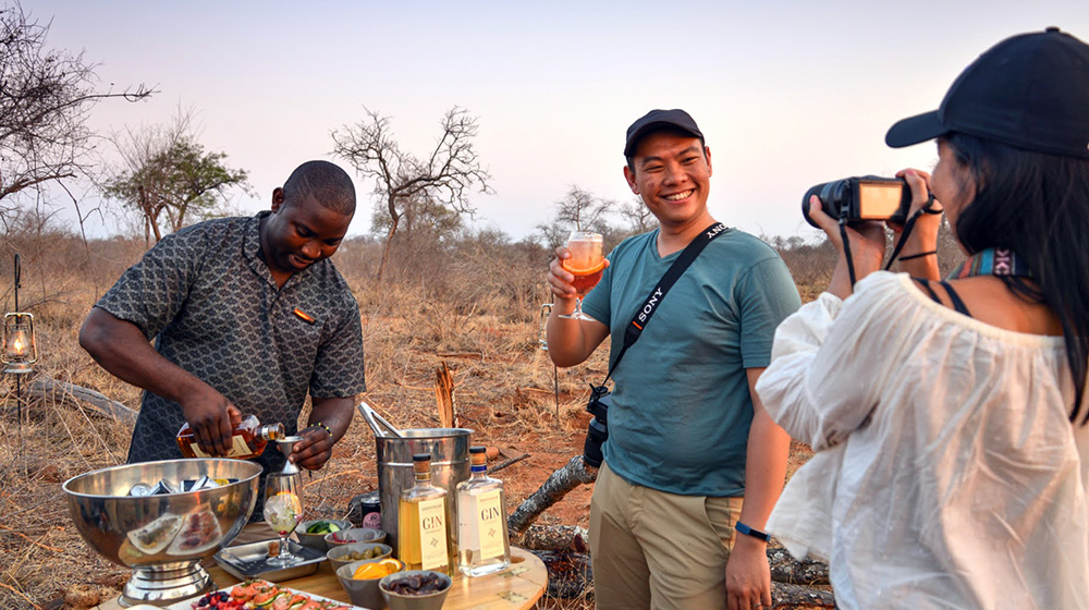 Couple on safari having a photo taking with man making drinks for them