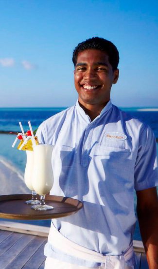 Waiter on tropical island holding tray of cocktails